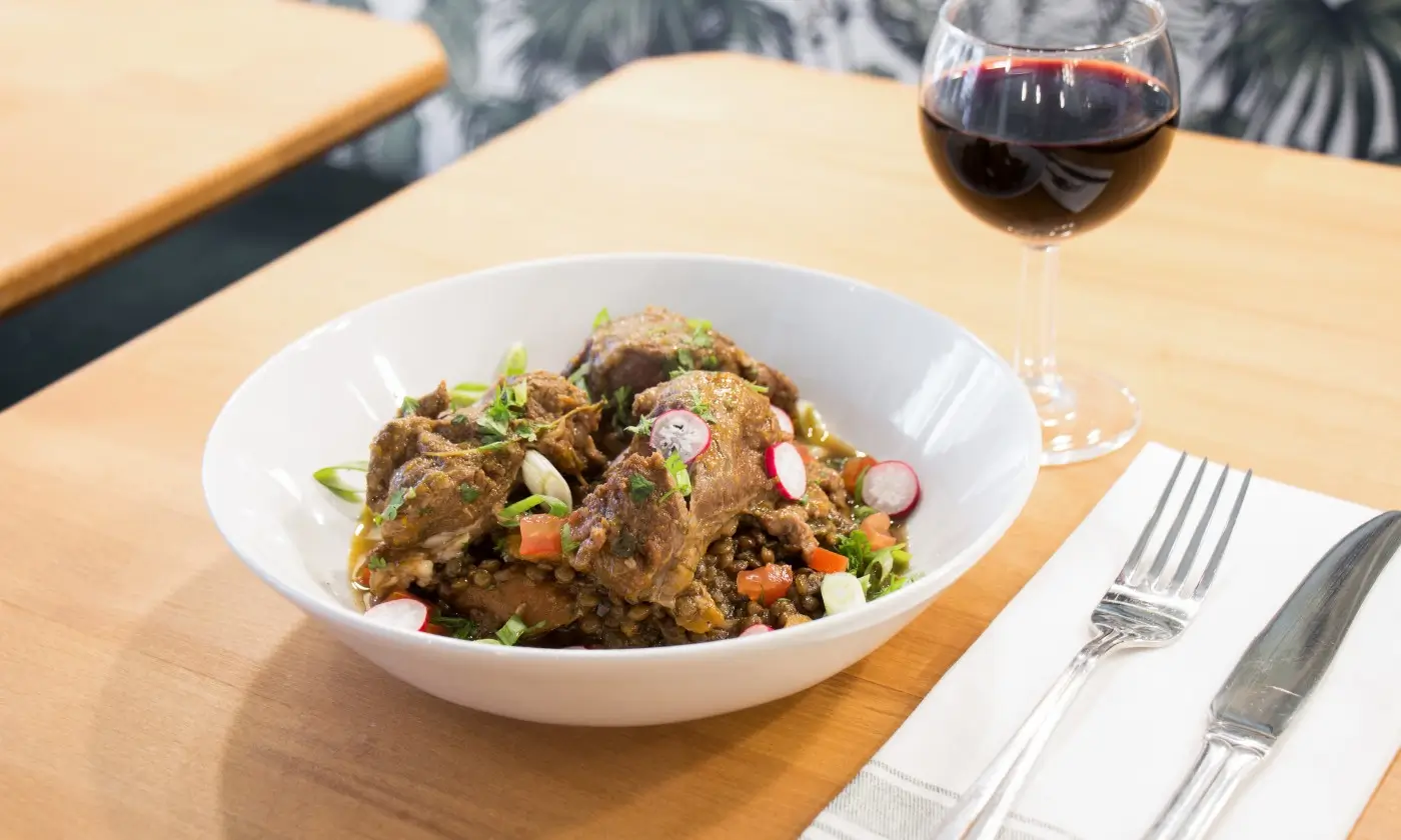 A dish at Bistrot Rougemont, Paris, presenting braised meat with lentils and fresh vegetables, paired with a glass of red wine on a wooden table.