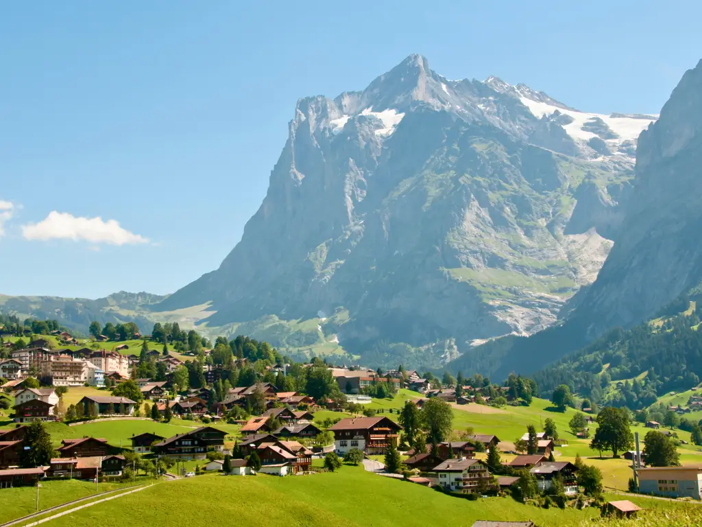 The idyllic town of Grindelwald, Switzerland, nestled in green valleys with traditional chalets dotting the landscape and the majestic Eiger Mountain rising in the backdrop on a sunny day.