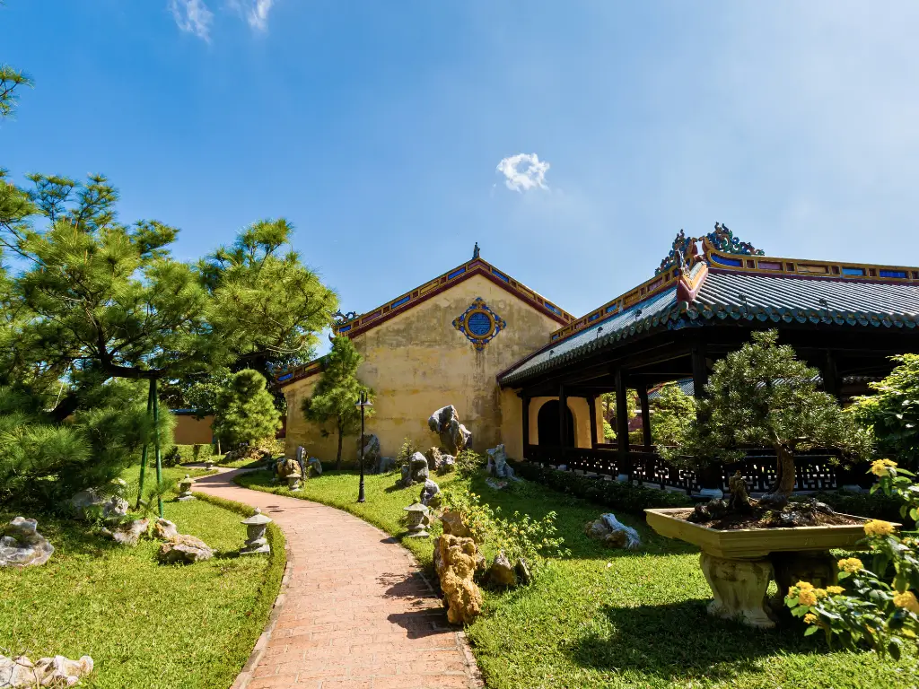 Path leading through a tranquil garden in Hue, Vietnam, with classical Eastern architecture, embodying the peacefulness of slow travel destinations.