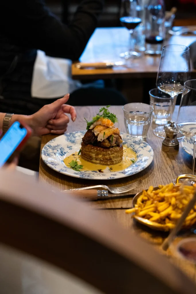 A patron at Le Bon Georges bistro in Paris enjoys a meal of layered vegetable terrine topped with shrimp, served on a patterned plate, with a side of fries and a glass of red wine.