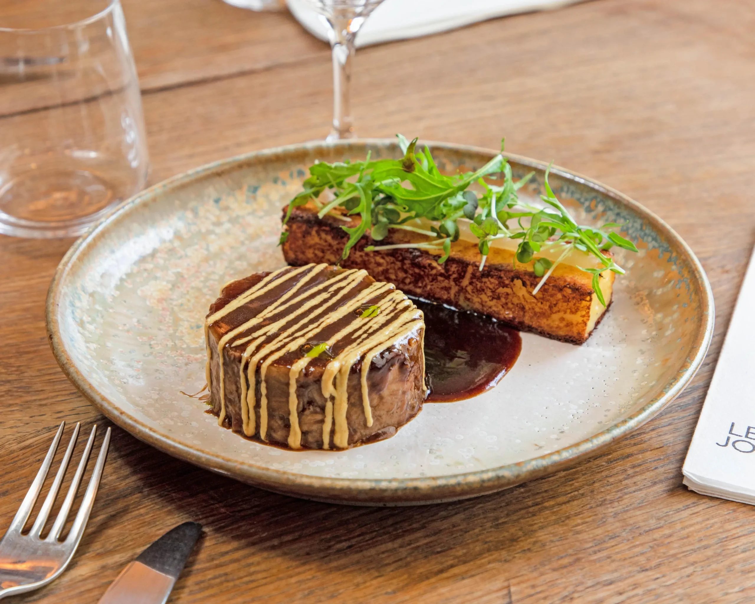 A plate of meat dish with garnish on a wooden table at Le Jourdain, a French bistro in Paris.