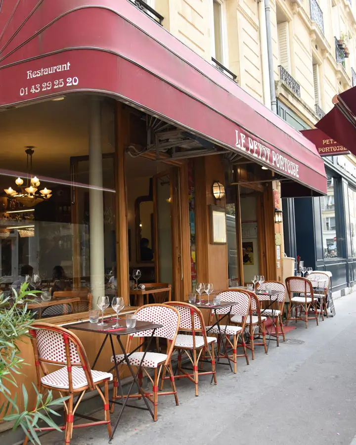 Charming street-side dining at Le Petit Pontoise with red and white rattan chairs, reflecting the quaint and casual elegance of Paris bistro culture.