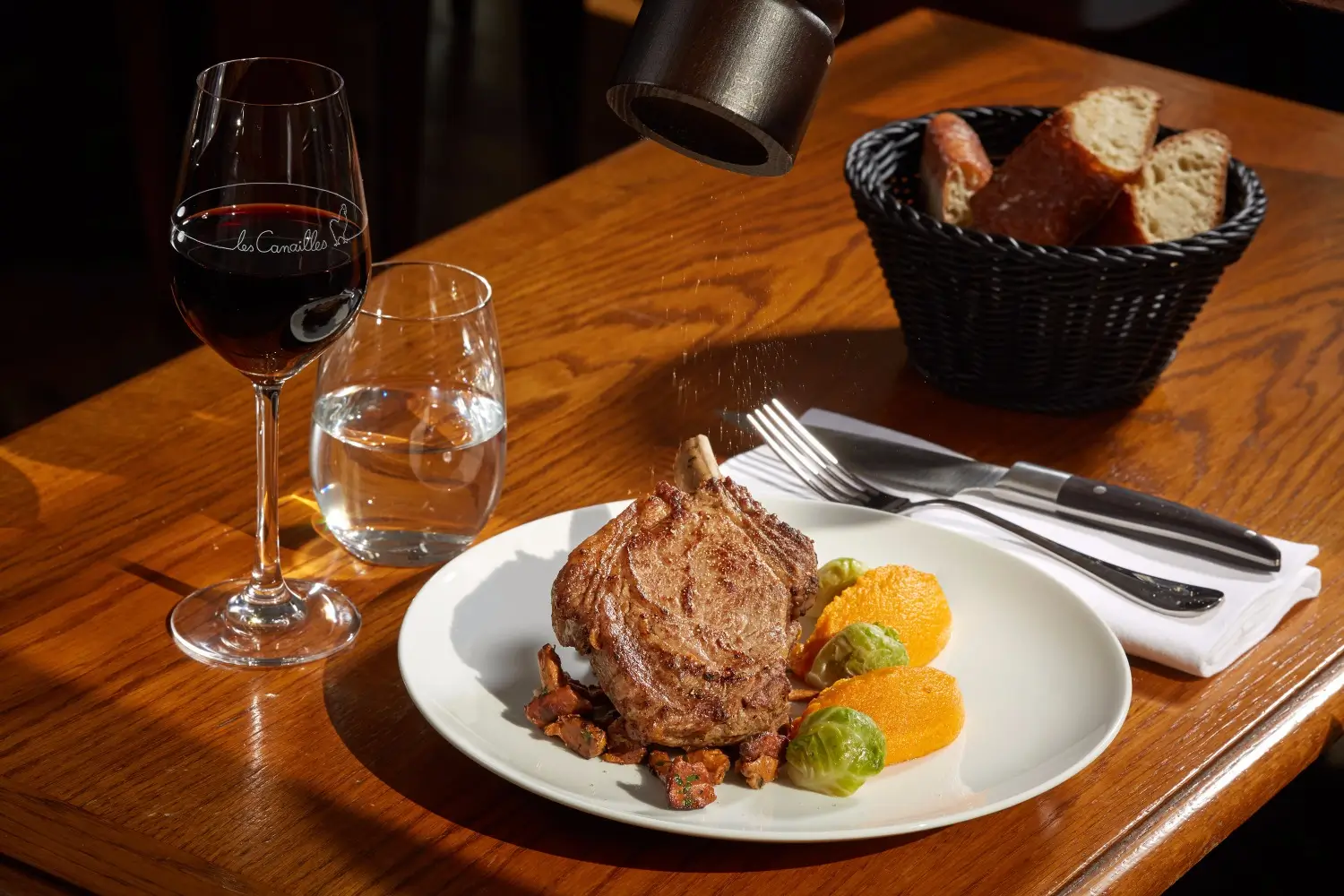 A perfectly cooked steak served with root vegetables on a white plate at Les Canailles bistro in Paris, paired with a glass of red wine, creating an inviting meal setting.