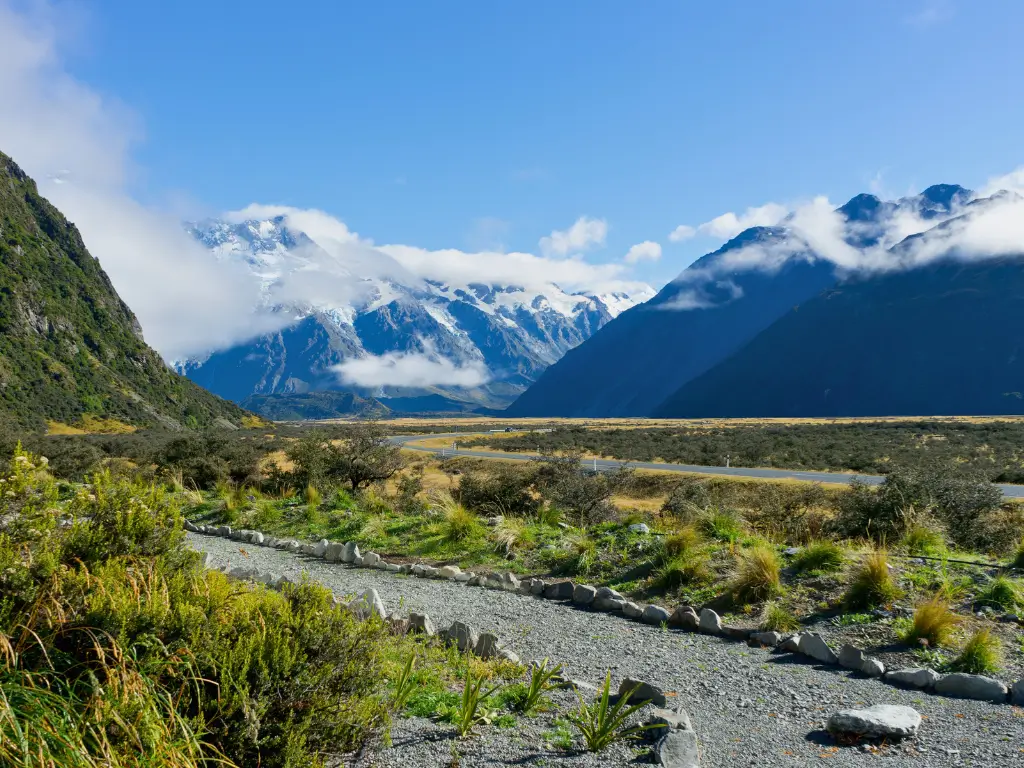 A peaceful path winds through a dramatic landscape with towering mountains and low-hanging clouds in New Zealand, encapsulating the essence of slow tourism destinations.