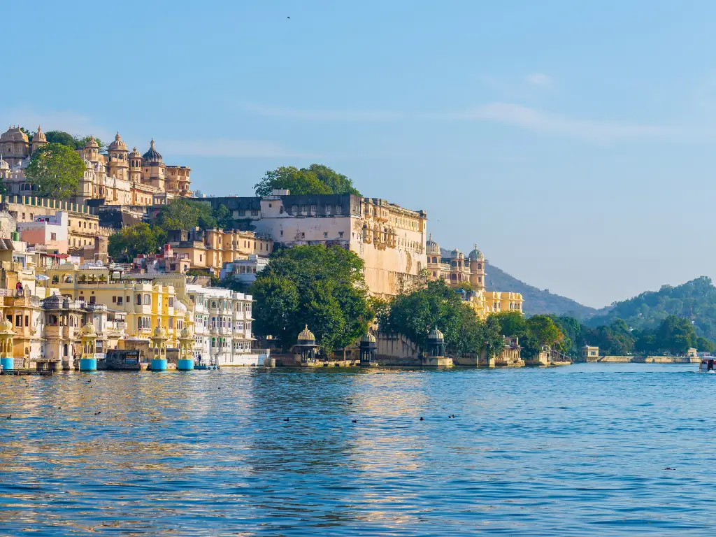 Majestic waterfront palaces reflecting the rich history of Rajasthan, India, against a clear blue sky. It's inviting travelers to immerse slowly in the destination's culture.