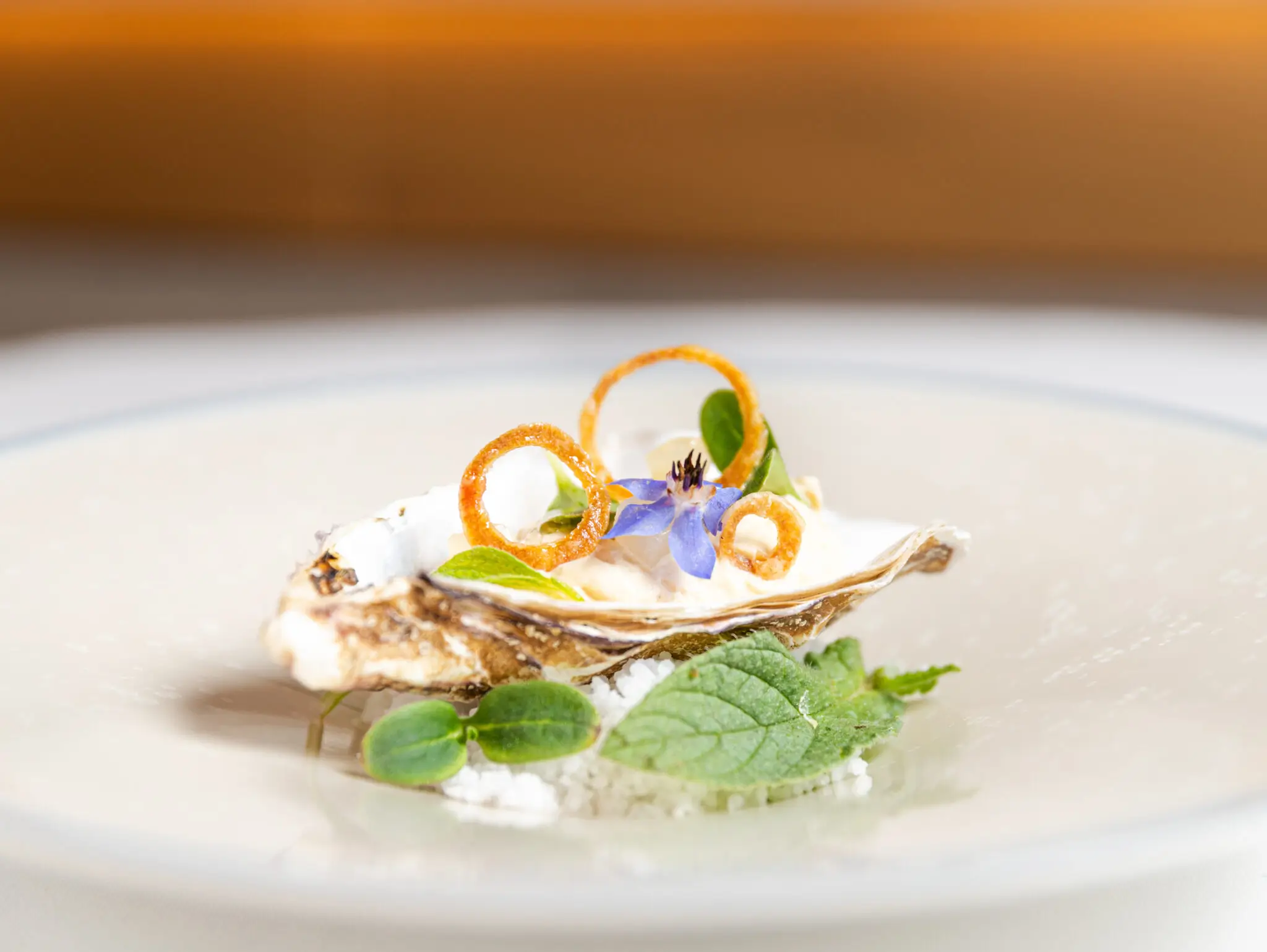 A freshly served Kermancy oyster at Restaurant Alliance in Paris, elegantly garnished with herbs, flowers, and a citrus twist, resting on a bed of ice – showcasing the affordable finesse of Michelin-starred cuisine."