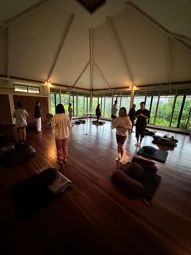 Evening meditation session with attendees in white clothing inside a spacious, well-lit yoga studio, capturing the tranquil ambience of silent meditation retreats in Bali.