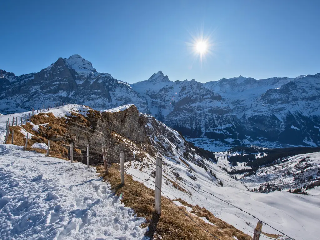 Bright sun shining above the snow-covered slopes of the ski area in Grindelwald First, with the rugged peaks of the Swiss Alps towering in the background,