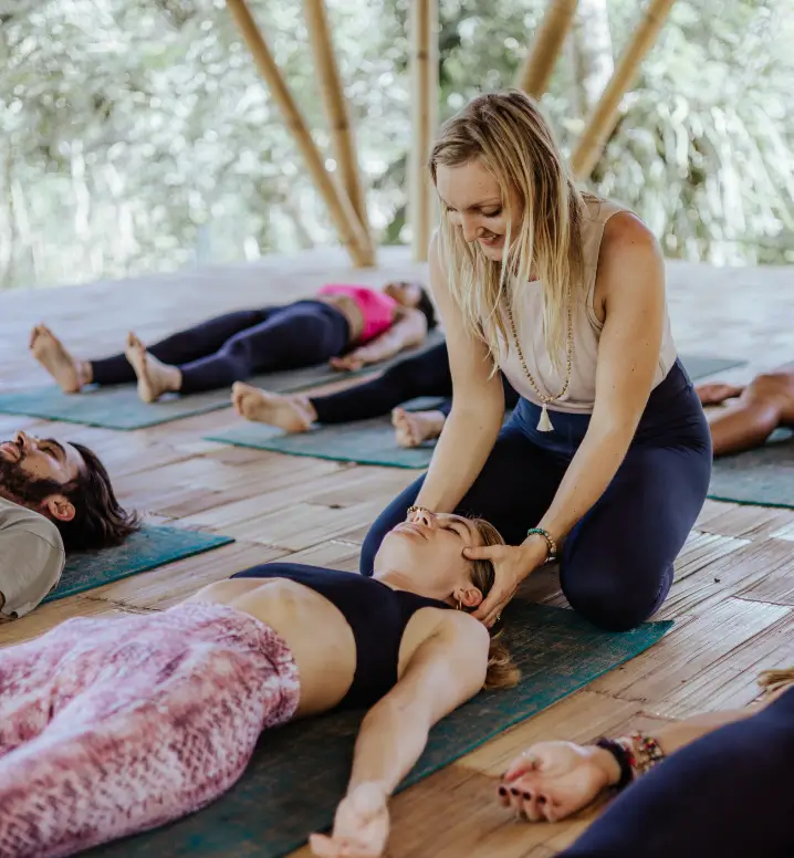 A yoga instructor at Surf & Yoga Canggu assists a participant in a relaxation pose, showcasing personalized care in wellness retreats in Bali.