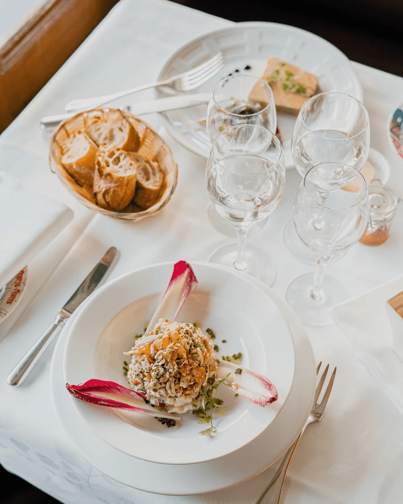 Elegant dining setup at Chez Georges with white linen-covered tables, polished glassware, and wooden bistro chairs, embodying the quintessential Parisian bistro experience.