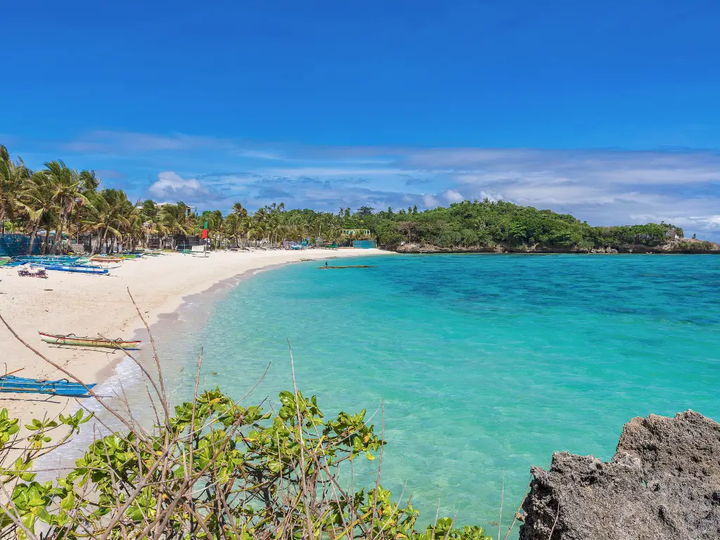 Crystal-clear turquoise waters meet the white sandy shores of Tambisaan Beach, framed by lush tropical greenery, a tranquil Boracay land tour destination