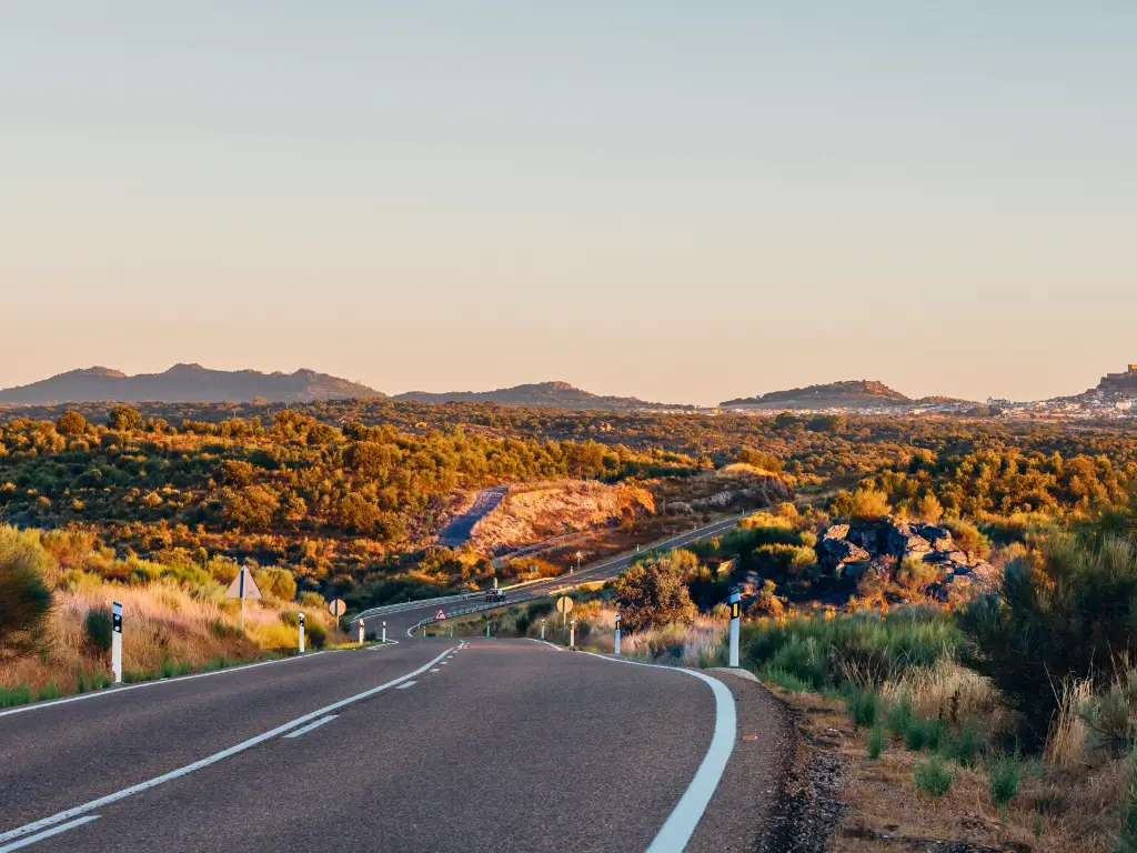Open road meandering through the golden countryside at sunset in The Alentejo, Portugal, inviting exploration at a leisurely pace typical of slow travel destinations.