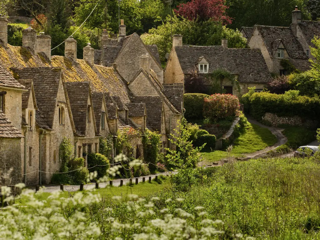 Quaint stone cottages with thatched roofs nestled in lush greenery in The Cotswolds, England, embodying the charm of slow travel destinations.