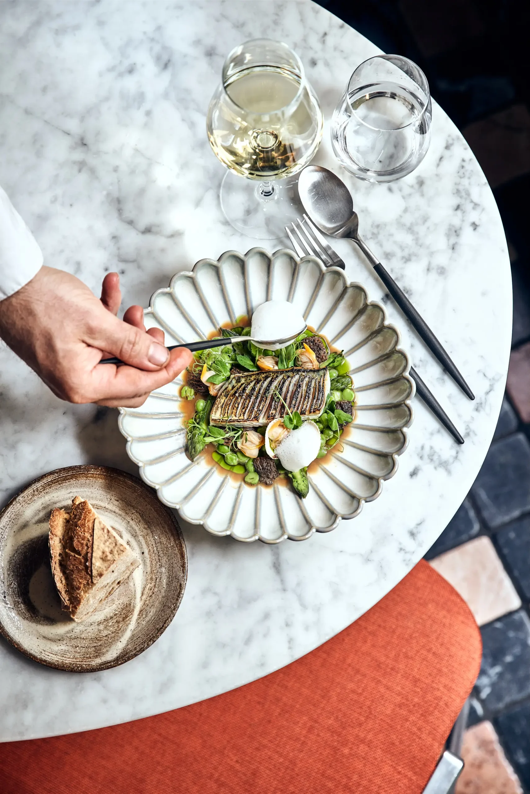 A gastronomic delight at Virtus, one of the cheapest Michelin Star restaurants in Paris , with a beautifully plated grilled fish adorned with fresh greens, a dollop of cream, and served with a glass of white wine and artisanal bread.