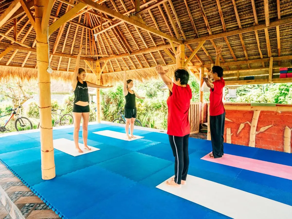 Group yoga session at Balitrees, one of the best yoga retreats in Bali. Participants are stretching under a traditional thatched-roof pavilion