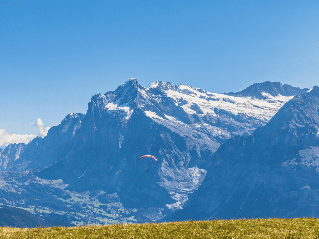 Paraglider soaring in the clear blue sky over Grindelwald with the Wetterhorn mountain’s snowy peak providing a breathtaking backdrop