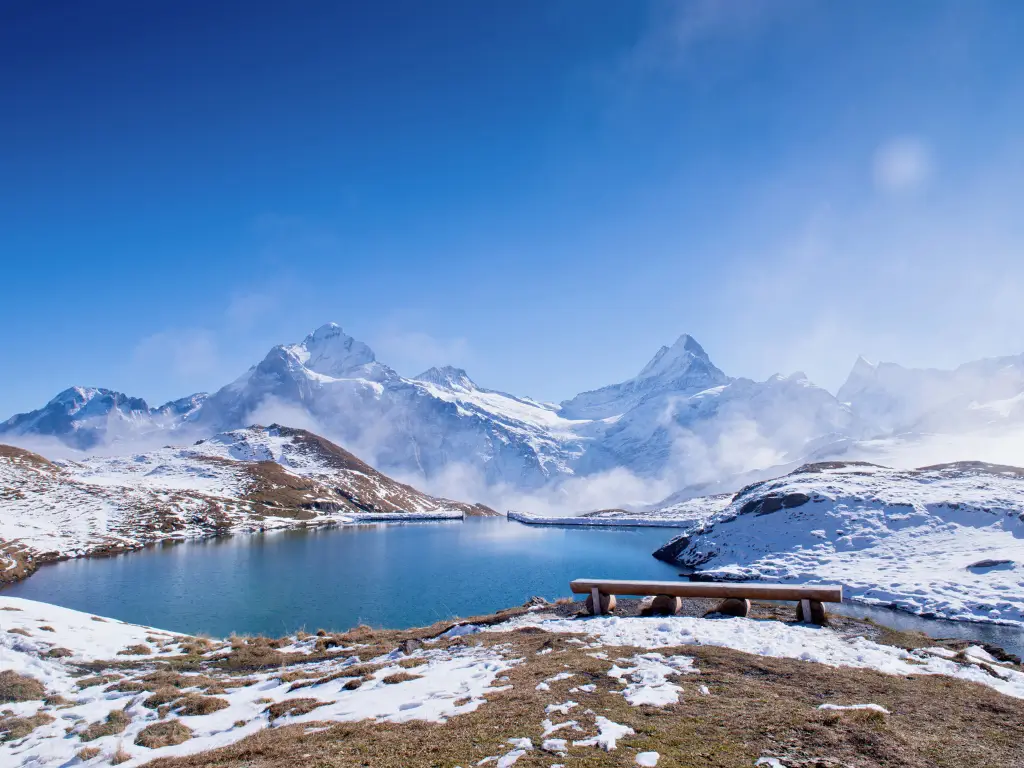 Lake Bachalpsee reflecting the Swiss Alps, with a wooden bench inviting hikers to rest and soak in the serenity.