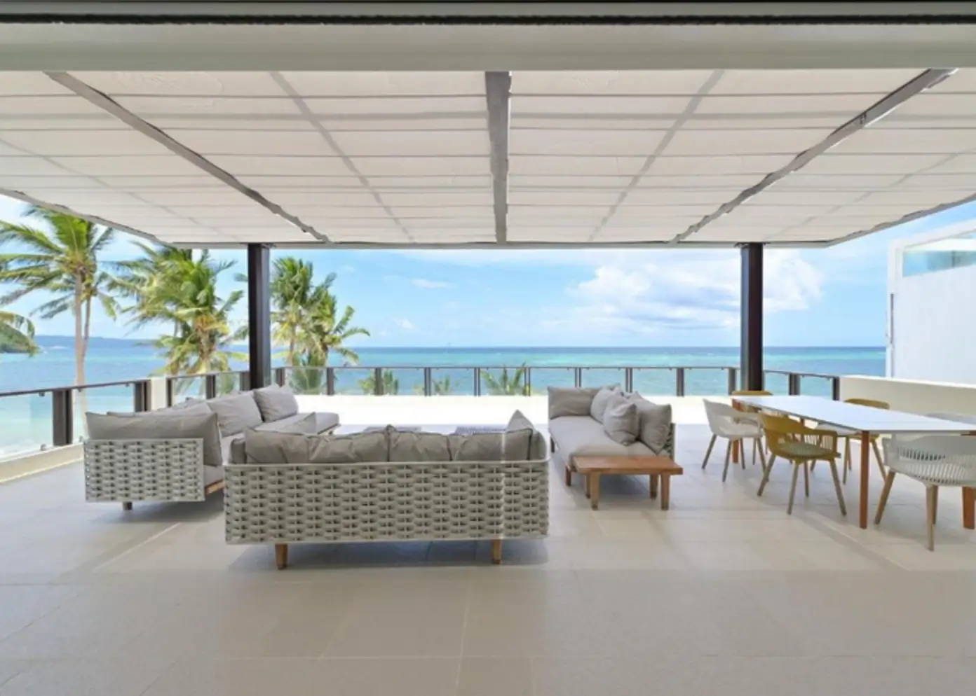 Open-air lounge area of the penthouse at 7Stones, a boutique hotel in Boracay. The space is stylishly furnished with modern sofas and a dining area, offering a panoramic view of the sea and palm trees.