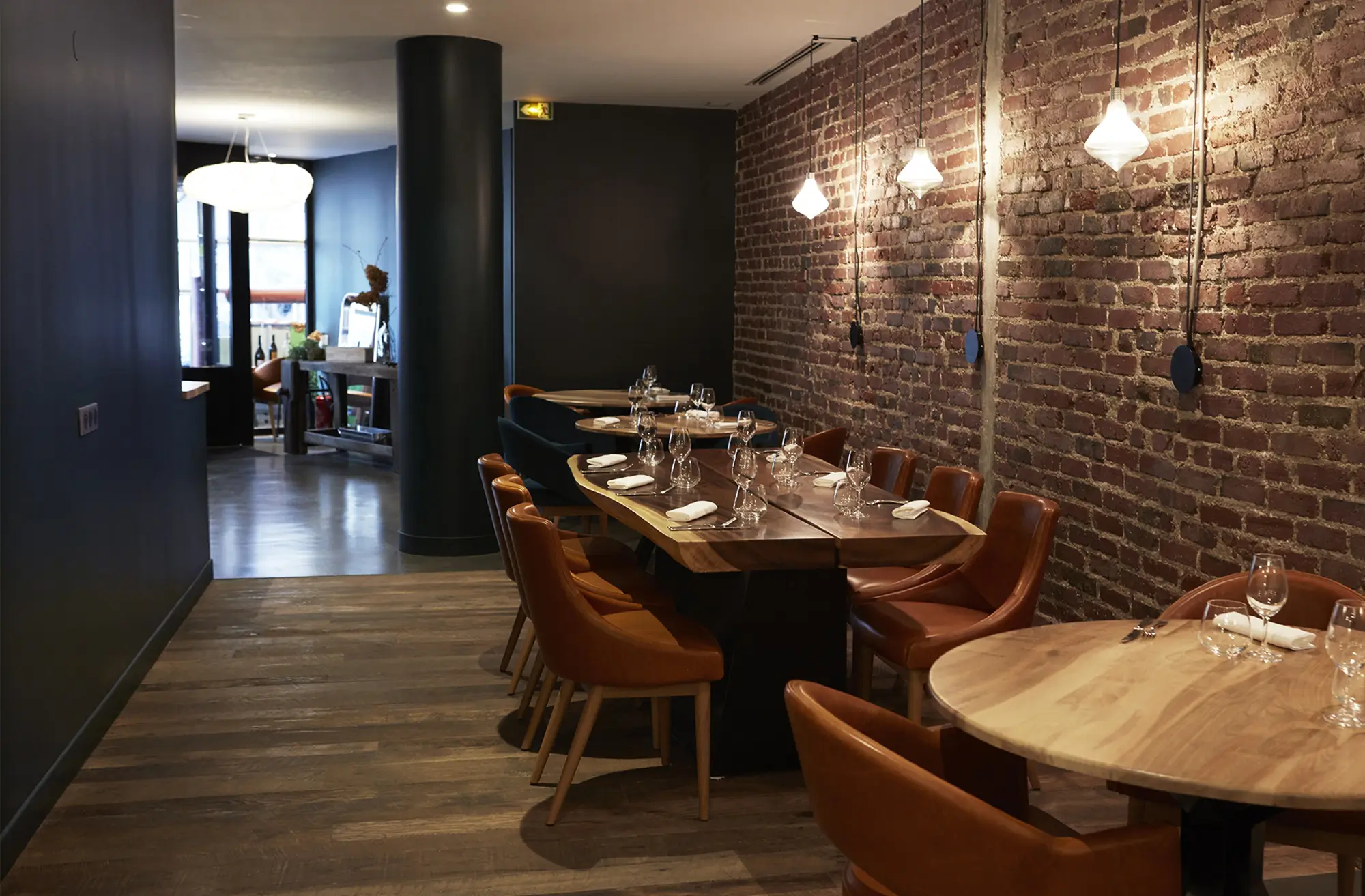 The interior of ACCENTS Table Bourse, an affordable Michelin star restaurant, featuring a dining area with exposed brick walls, modern pendant lights, and elegantly set tables with leather chairs.
