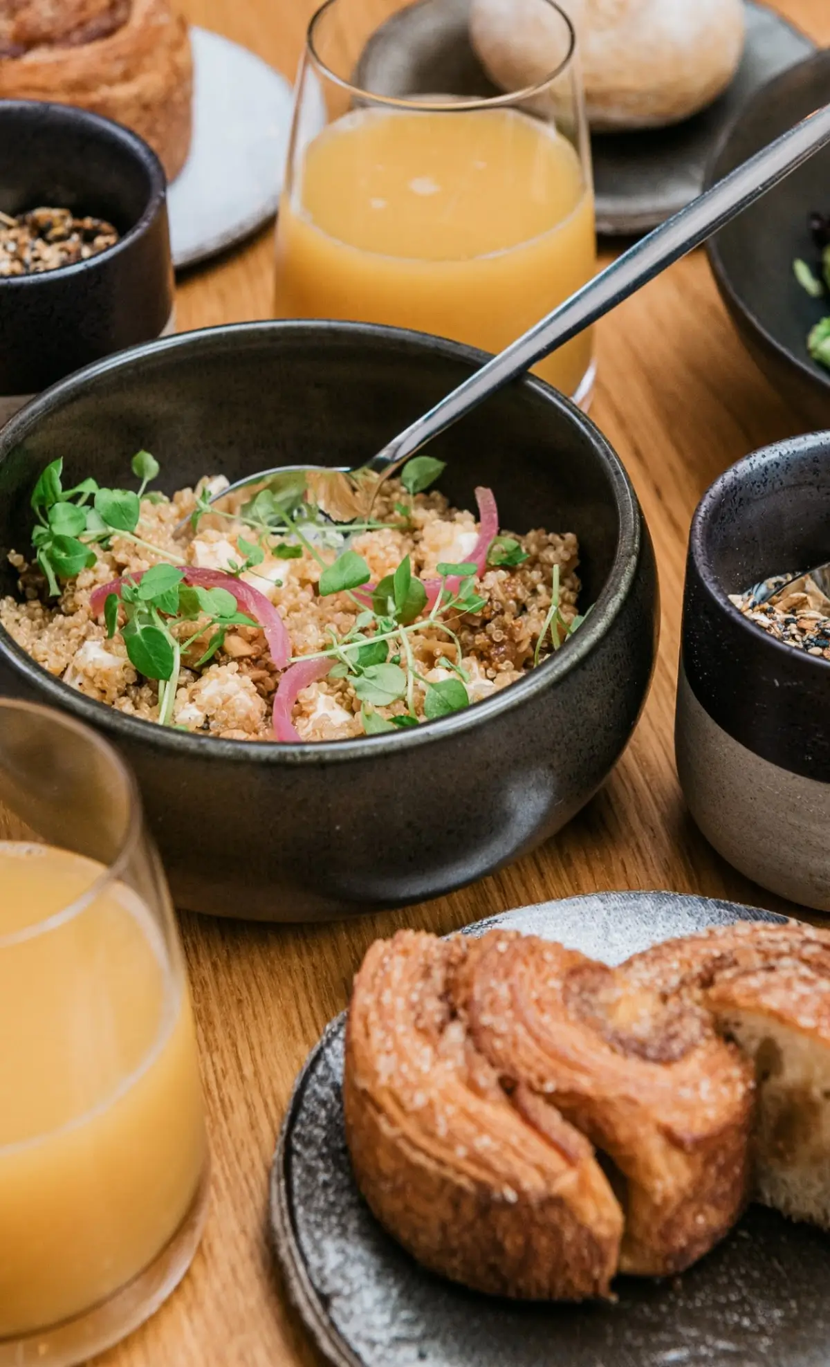 A breakfast spread at ANONA featuring a bowl of quinoa salad with microgreens, pastries, and glasses of orange juice. Highlighting the fresh and diverse menu at an affordable Michelin star restaurant in Paris.