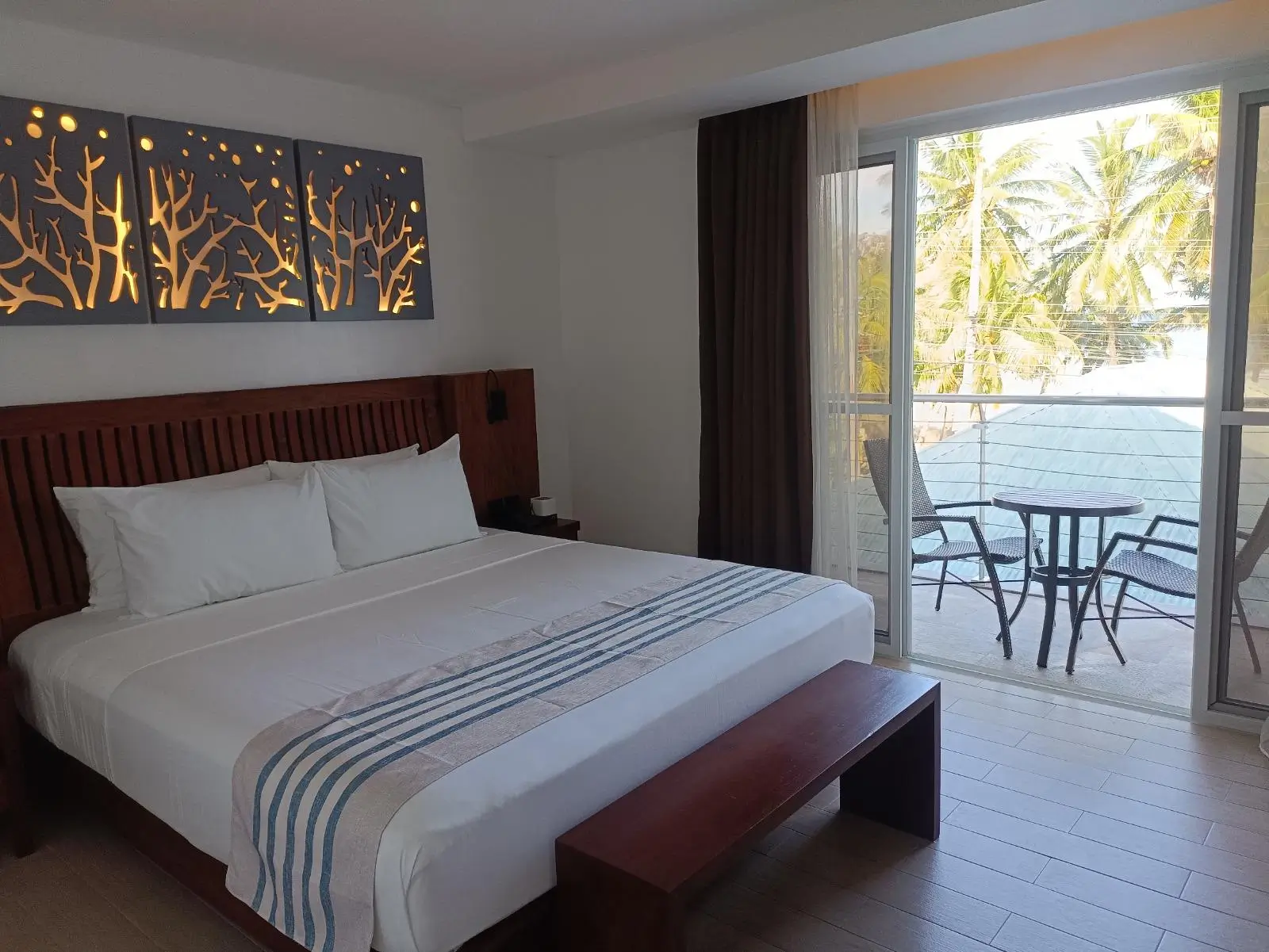 Elegant hotel room at Aira Boracay, a boutique resort in Boracay, with a spacious bed, wood-accented decor, and sliding glass doors that open to a balcony with a view of palm trees.
