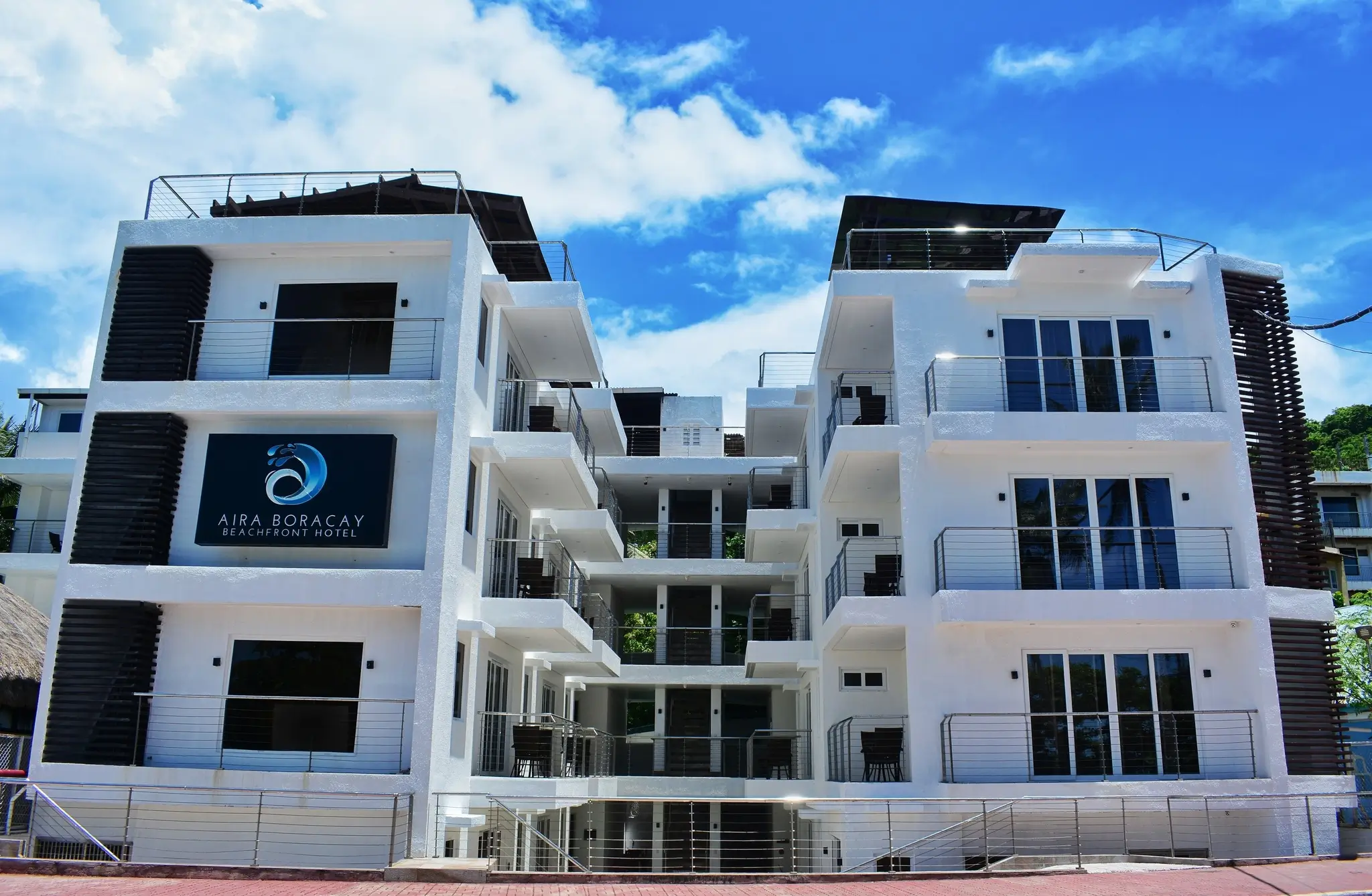 Exterior view of Aira Boracay, a boutique resort in Boracay, featuring a modern white facade with multiple balconies and sharp architectural lines. The building stands prominently against a bright sky, reflecting a contemporary beachfront aesthetic.