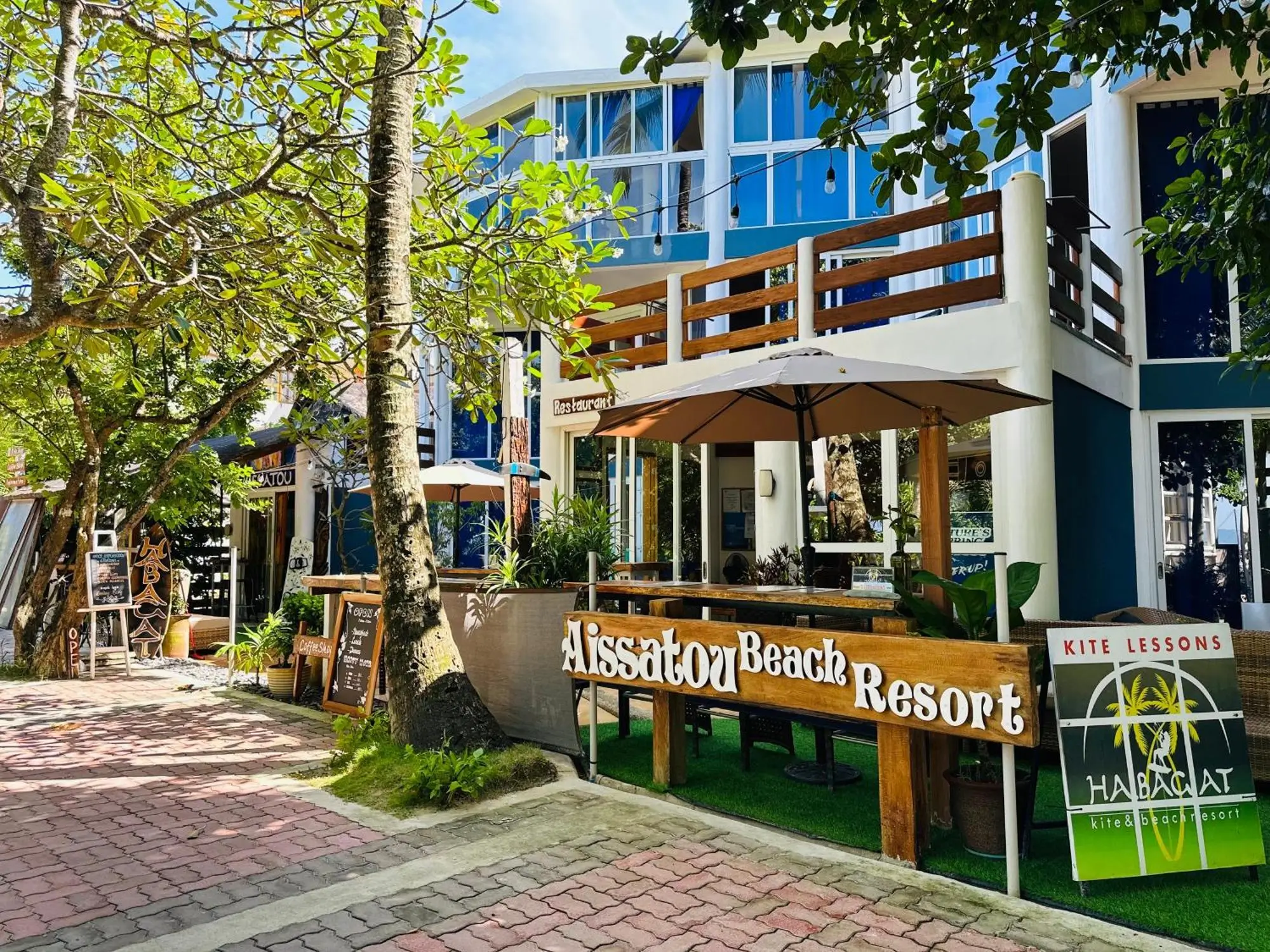 Front view of Aissatou Beach Resort in Boracay, displaying its charming exterior with a blend of modern and traditional design, wooden signboards for the resort and adjacent amenities, surrounded by lush greenery.