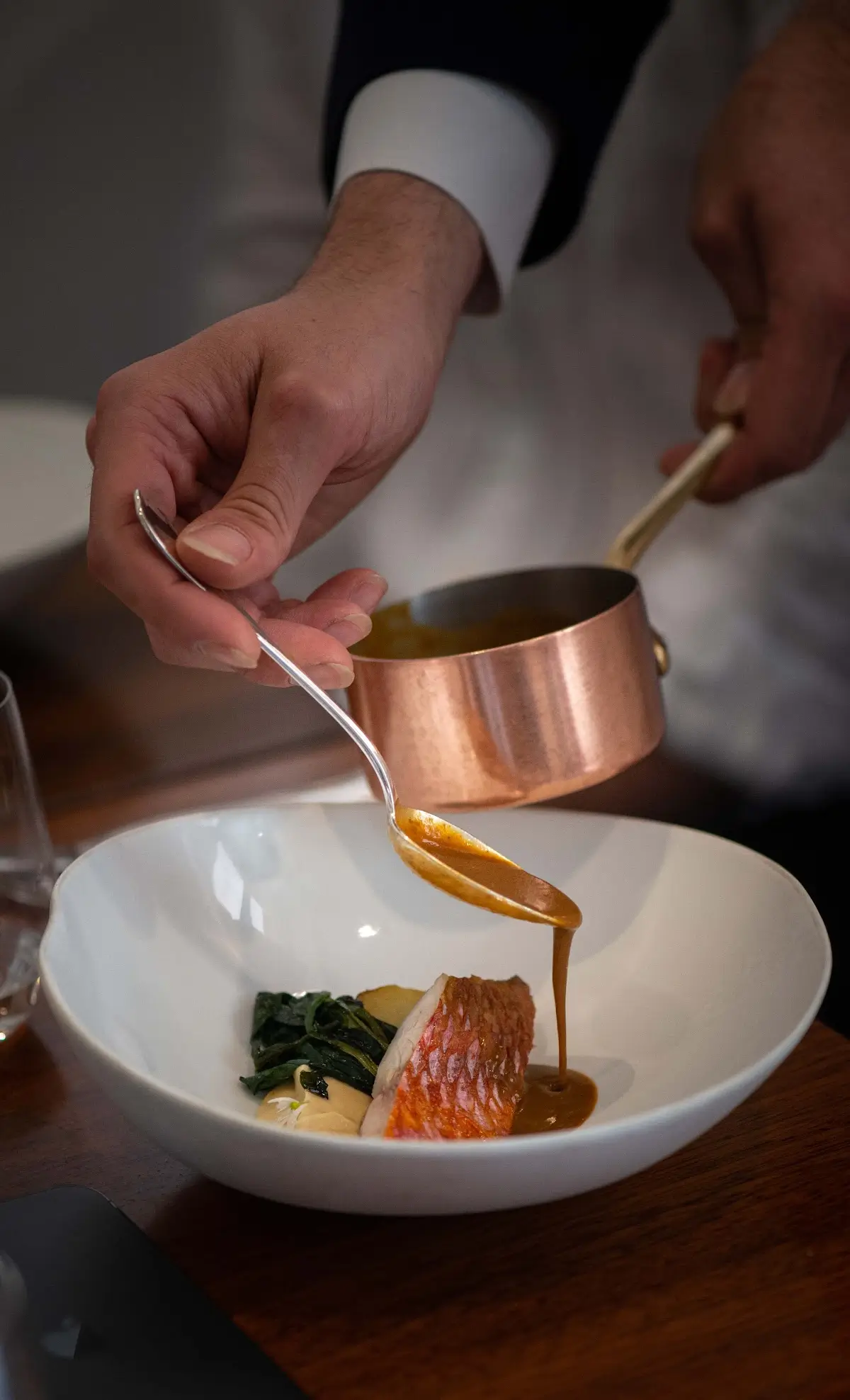 A chef pouring sauce over a gourmet dish at Automne, showcasing fine dining at an affordable Michelin star restaurant in Paris.