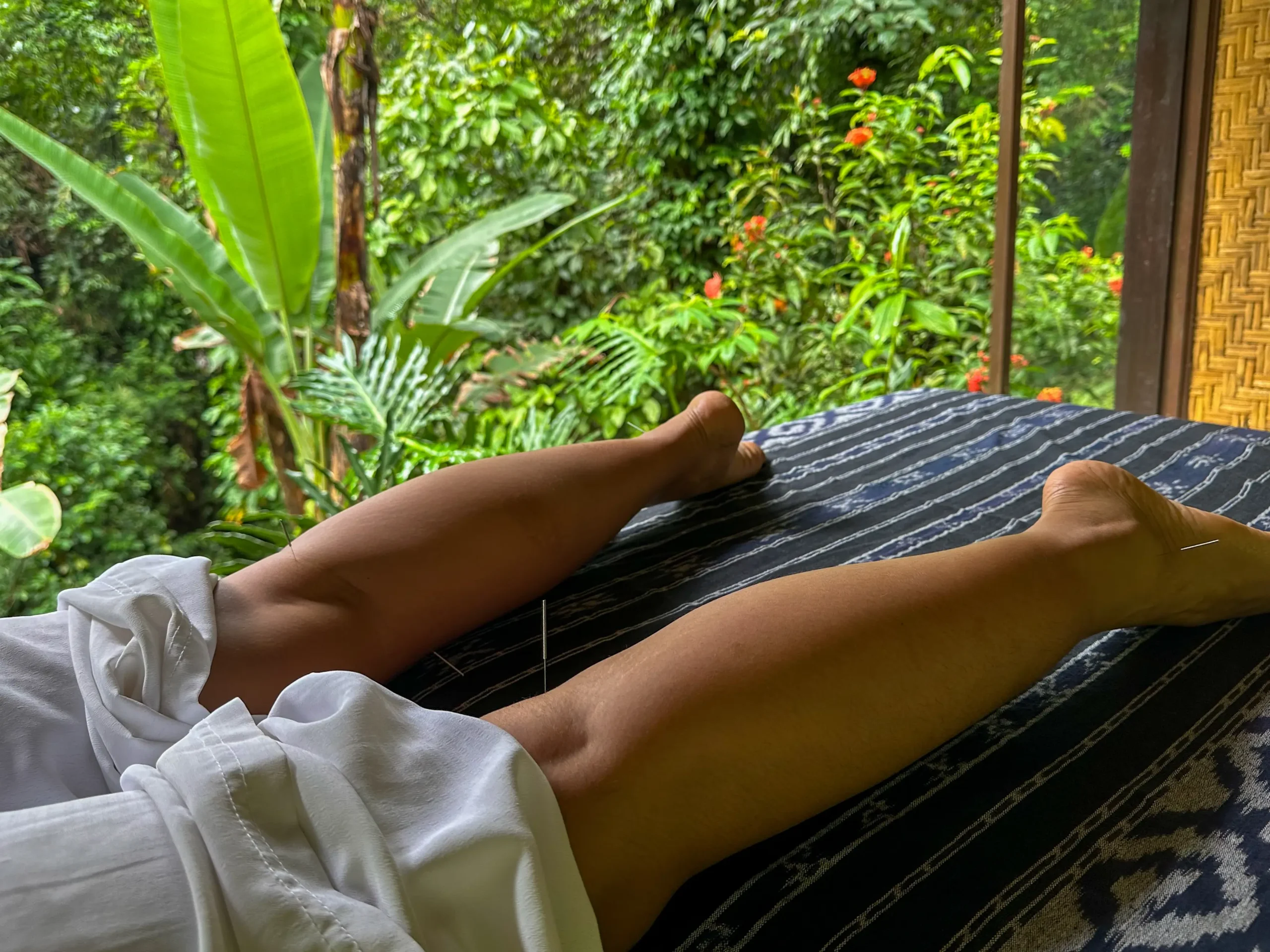 Close-up view of my legs stretched out on a massage table, overlooking a dense tropical forest from an open-air pavilion in Bali