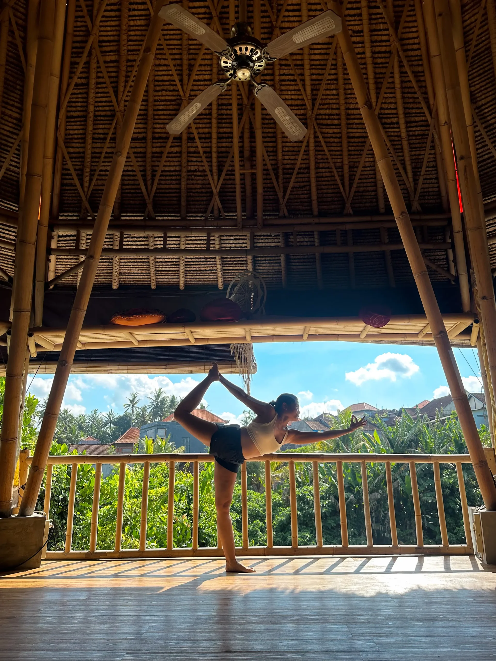 Me in a dancer's pose,balancing gracefully in a spacious, open-air bamboo pavilion at a yoga retreat in Bali. 