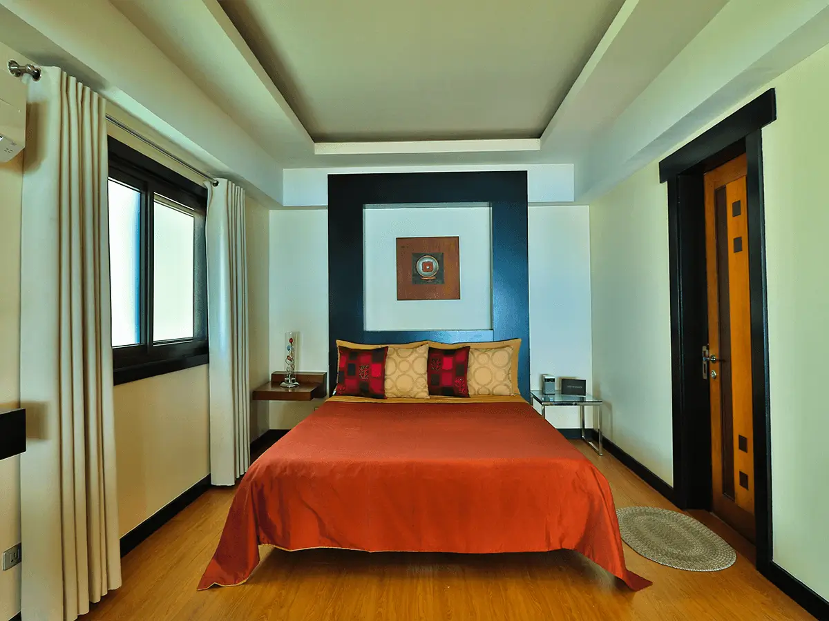 Bright and modern bedroom at Boracay Beach Houses, showcasing a bold red bedspread and stylish artwork, enhancing the boutique hotel's charm.