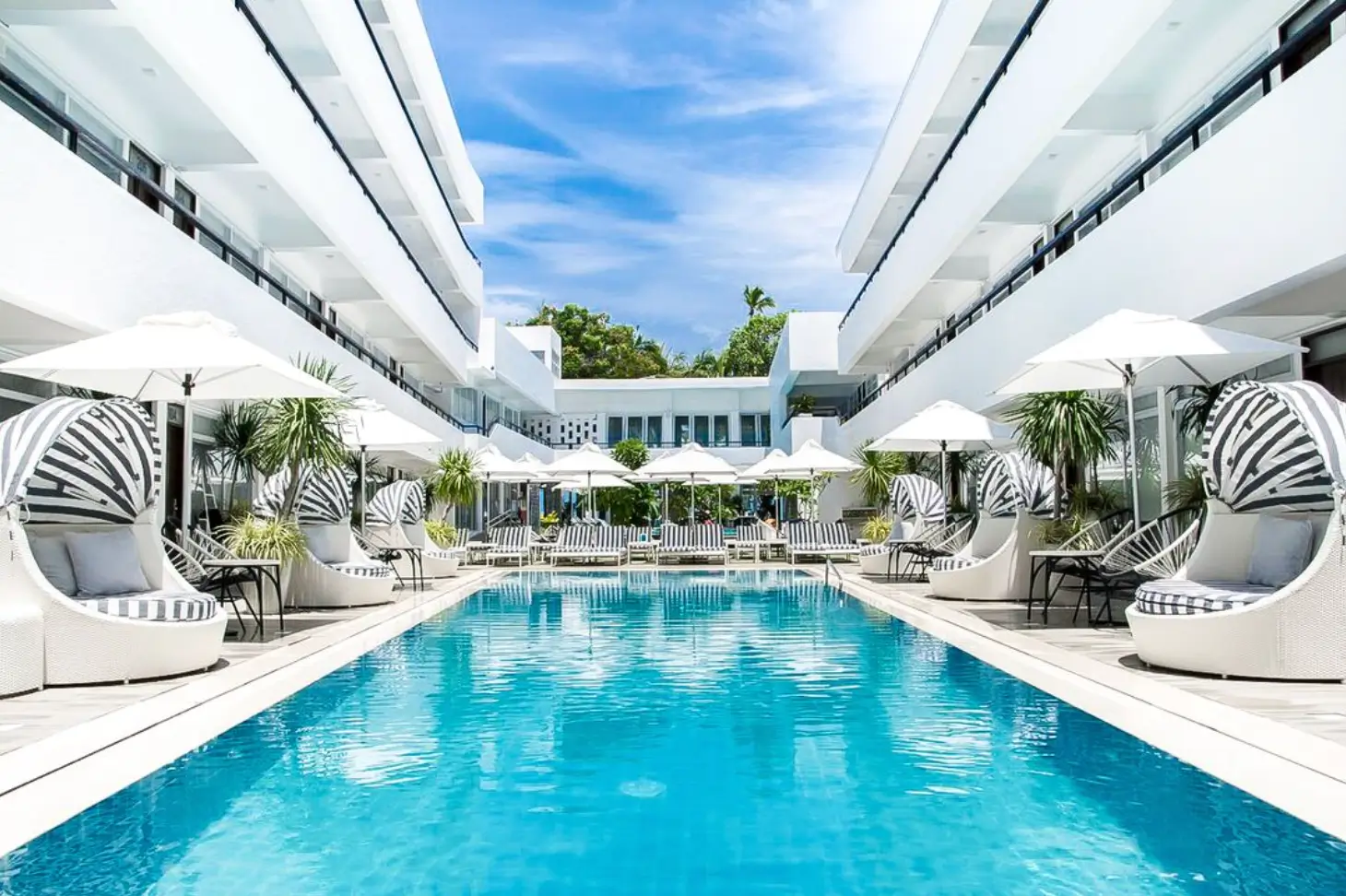Elegant pool area at Coast Boracay, lined with stylish cabanas and sun loungers under white umbrellas. The white, modern architecture of the hotel surrounds the pool, enhancing the luxurious tropical atmosphere.