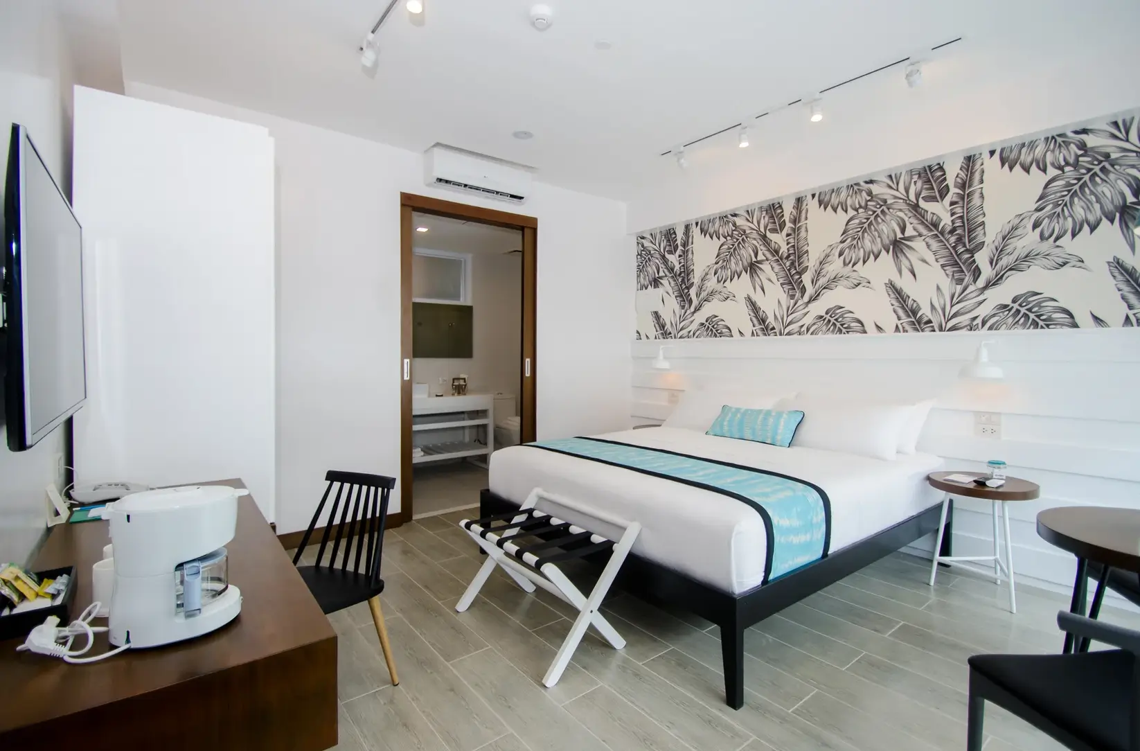 Spacious premiere room at Coast Boracay, decorated with a large bed against a botanical print wall. The room includes modern furniture, such as a sleek black bench and a small work area, providing both comfort and style.