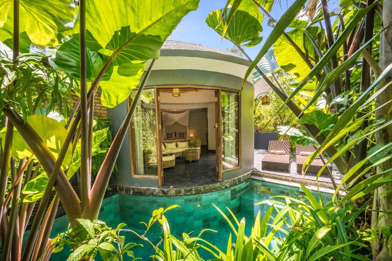A luxurious villa at De Moksha, an eco-friendly boutique wellness resort in Bali, surrounded by lush greenery and featuring a private blue pool.