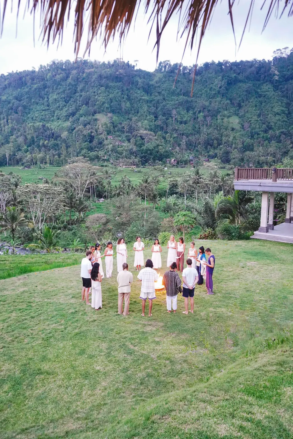 A group of participants forms a circle during a guided activity on a grassy field at a spiritual retreat in Sidemen, Bali.