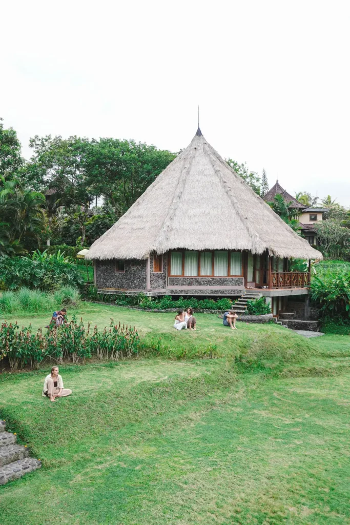 A traditional Balinese hut with a thatched roof, located in a green garden at a spiritual retreat in Bali.