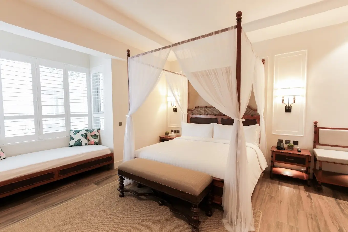 Charming and cozy bedroom in Feliz Hotel, a boutique hotel in Boracay, with a king-sized four-poster bed draped with sheer fabric, accented with rich wood furniture and tropical-themed cushions.