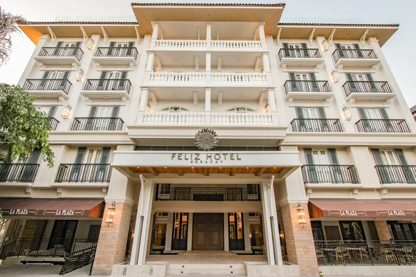 Front view of the elegant Feliz Hotel Boracay, showcasing a grand white facade with multiple balconies and a stately entrance flanked by columns. The hotel's architecture features classic design elements, providing a luxurious and welcoming atmosphere typical of top-tier boutique hotels in Boracay.