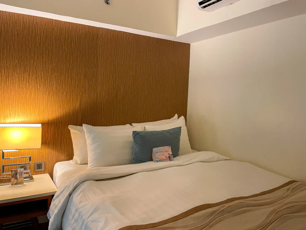 Minimalist bedroom at Ferra Hotel and Garden Suites, a boutique hotel in Boracay, featuring a wooden headboard and soft, neutral bedding.