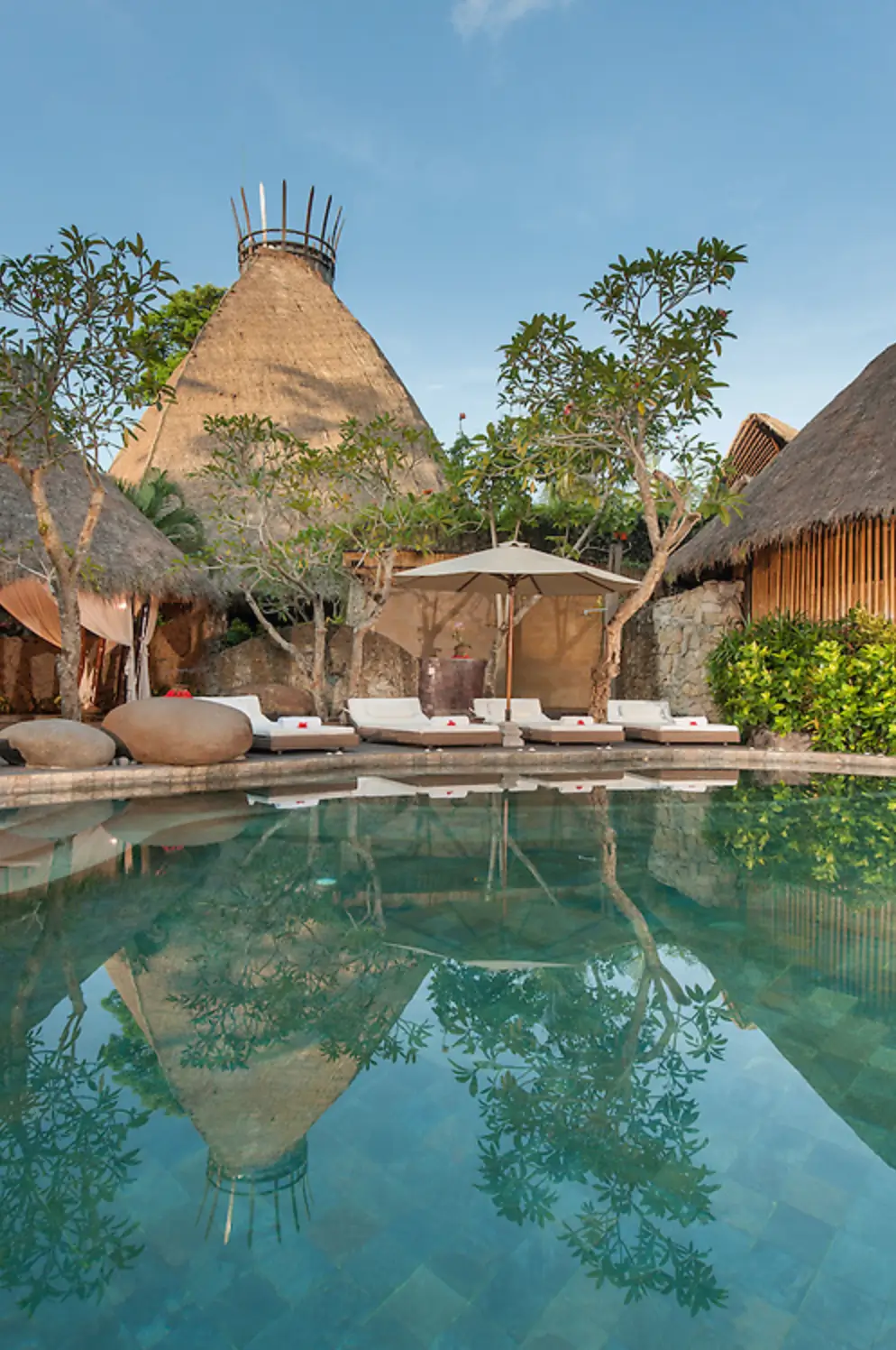 A tranquil pool area at Fivelements Retreat in Bali, featuring unique thatched-roof structures and comfortable lounging areas.