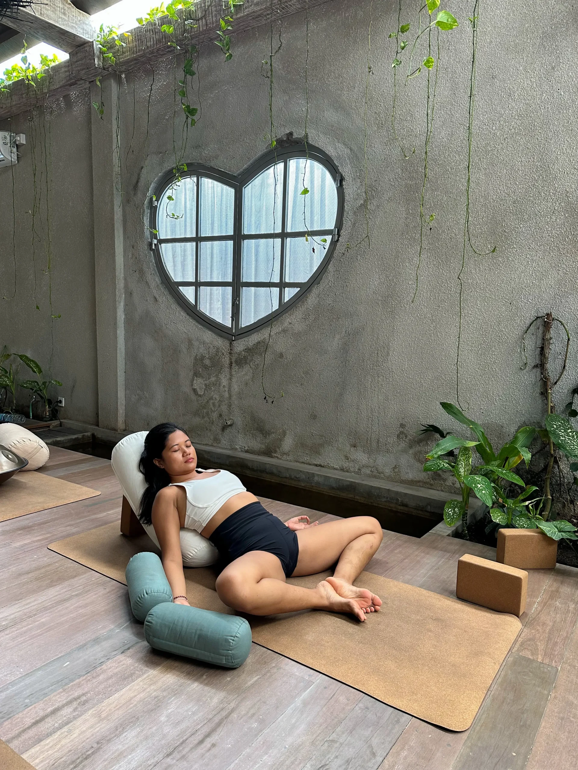 I relax in a reclined yin yoga pose using supportive bolsters in a serene, urban-style yoga space at Heart Space Bali. 