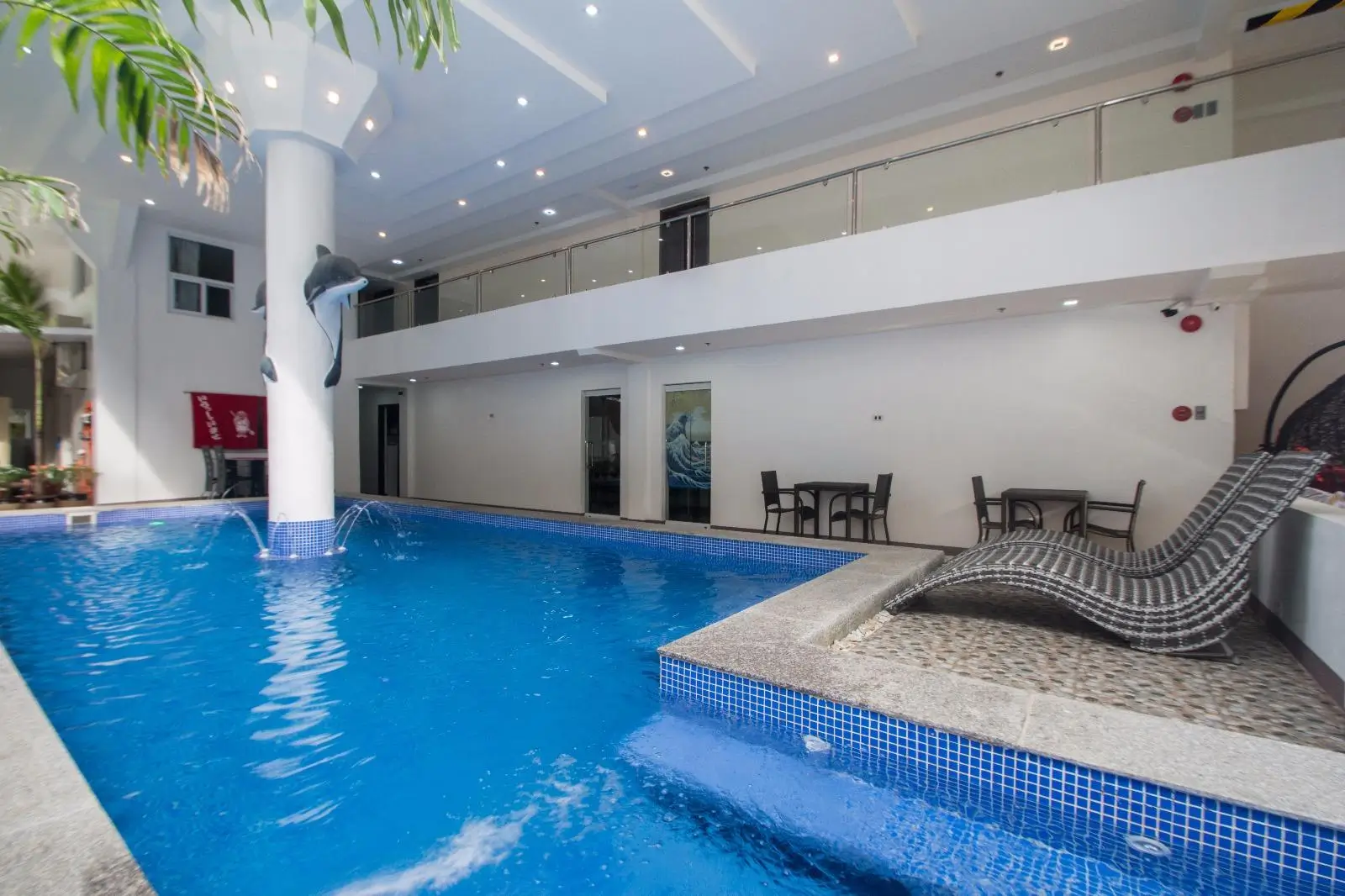 Indoor swimming pool at IL Mare Sakura Resort, a boutique hotel in Boracay, featuring a dolphin sculpture leaping from a central column, surrounded by a blue-tiled pool and two-tiered lounging areas.