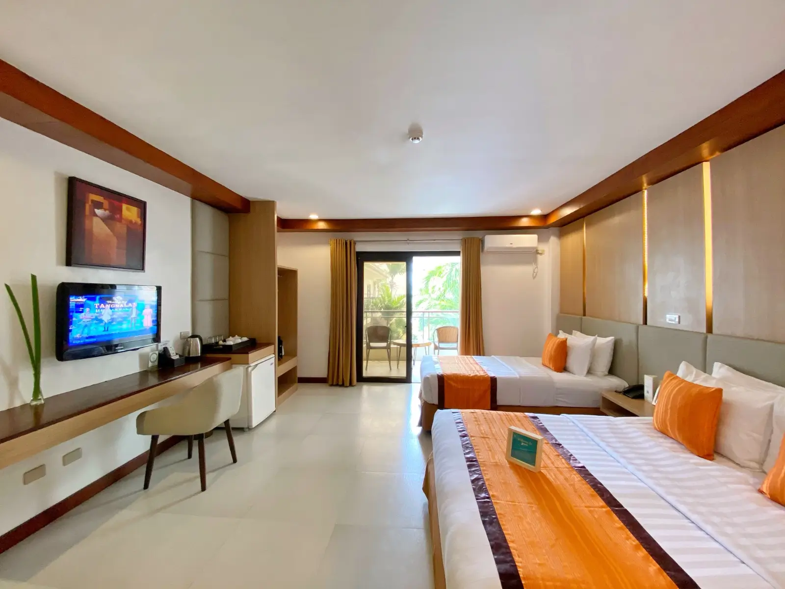 pacious guest room in Jony's Beach Resort featuring two large beds with crisp white and orange linens, a sleek wooden television console, and a view of the balcony.