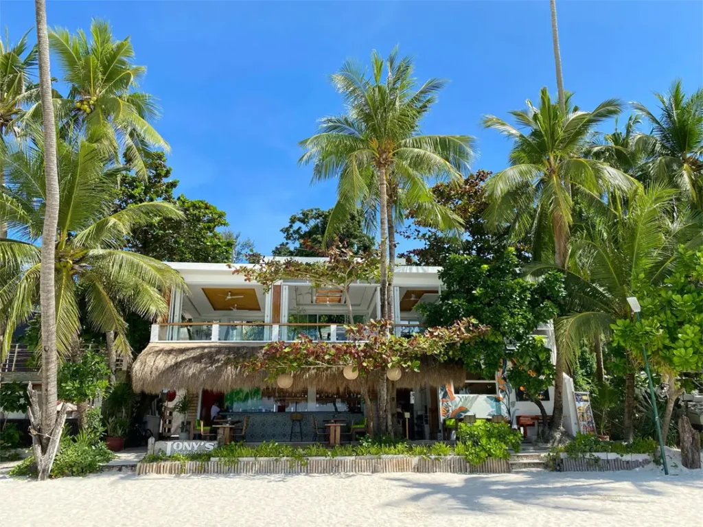 Front view of Jony's Beach Resort in Boracay, displaying a charming beachfront bar with a thatched roof and lush tropical palms surrounding the building.