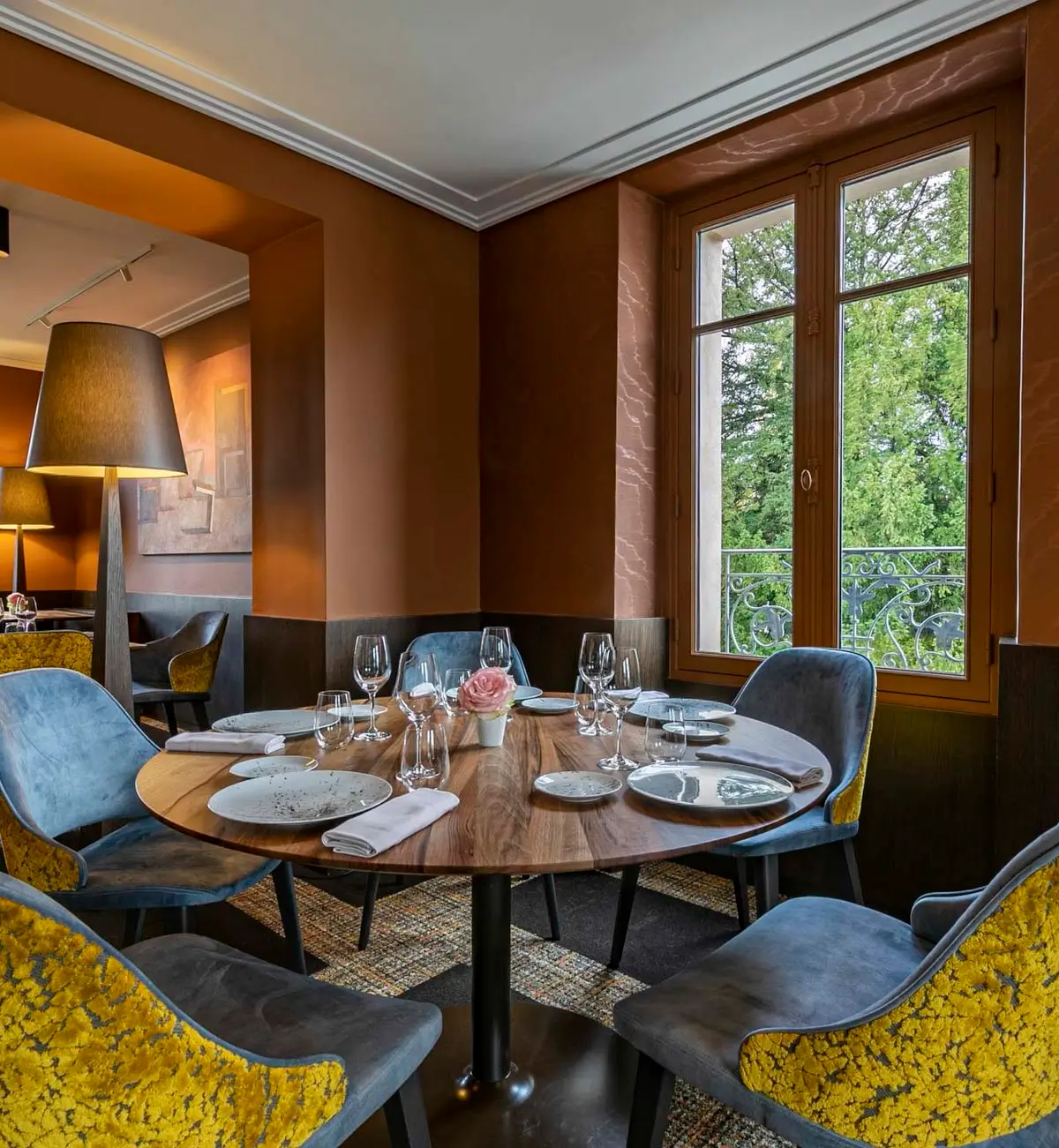 A cozy dining area at L’Escarbille, one of the affordable Michelin star restaurants in Paris, featuring a round table set for dining with elegant decor and large windows overlooking greenery.
