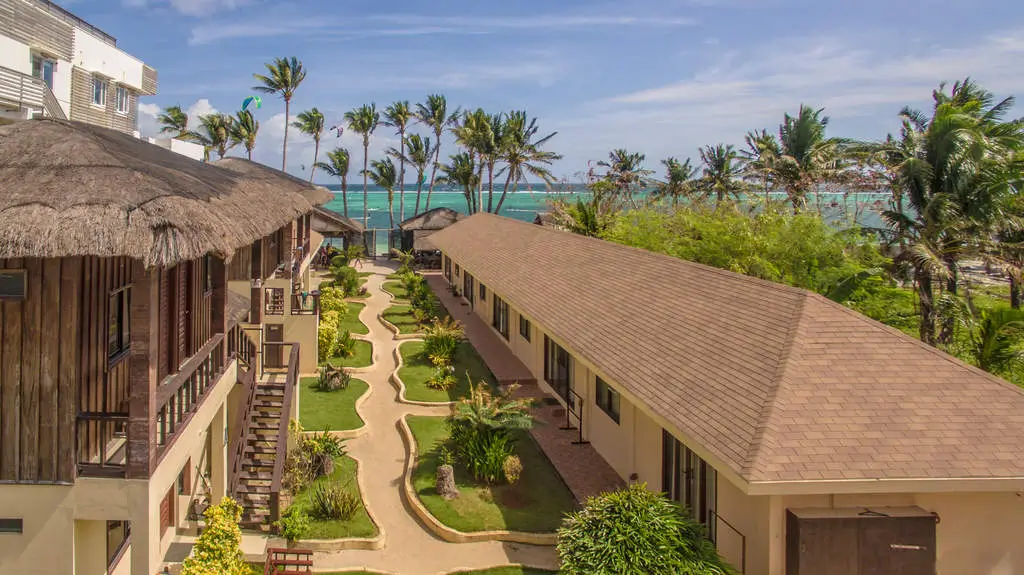 Aerial view of Levantin Boracay, one of the boutique resorts in Boracay, showcasing a mix of modern and traditional structures with thatched and tiled roofs nestled in a lush tropical garden leading to the beach, framed by palm trees against a turquoise sea backdrop.