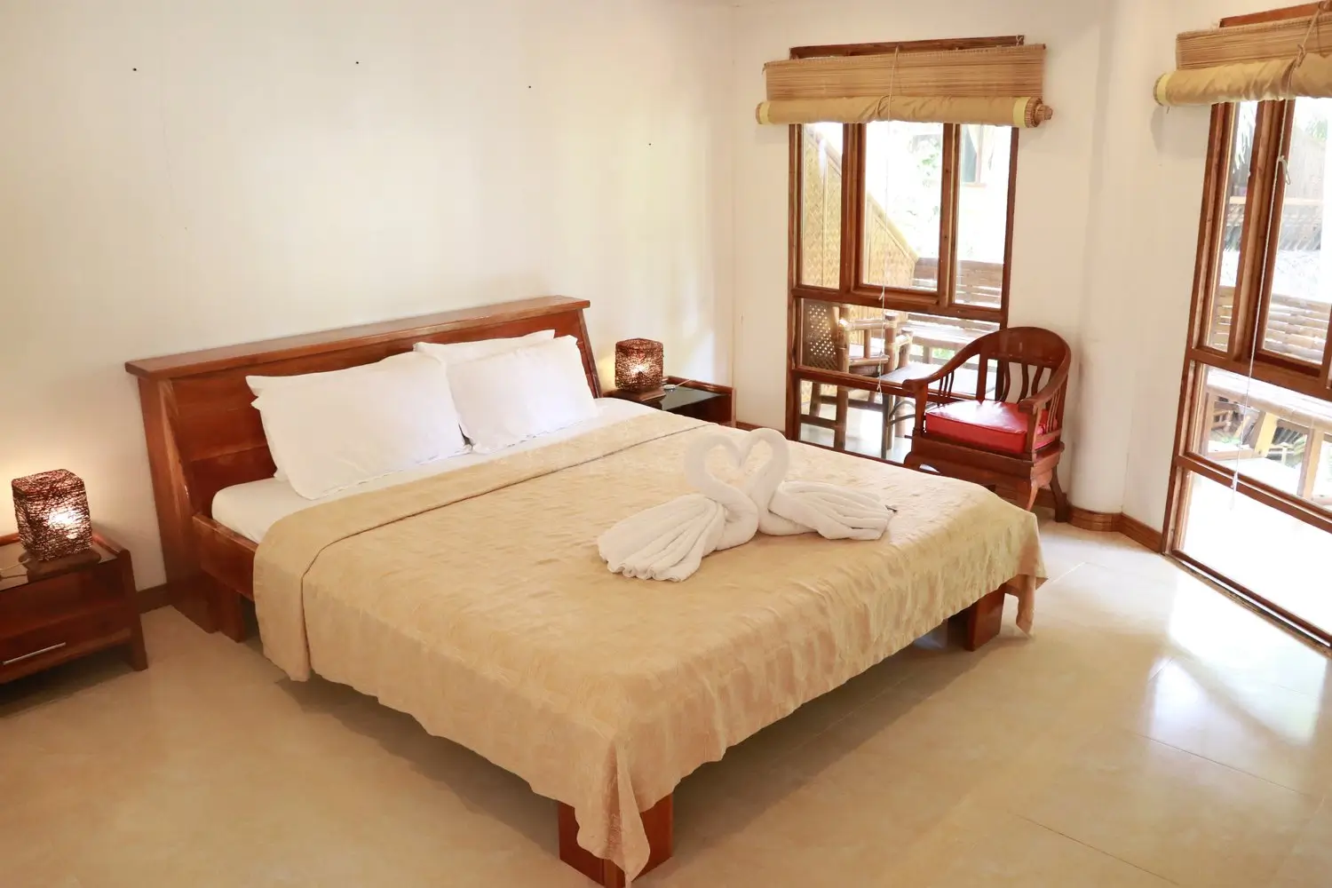 Bright and airy bedroom at Nigi Nigi Nu Noos Boutique Hotel in Boracay, featuring a queen-sized bed with white linens, wooden furniture, and towel art of two swans on the bed.