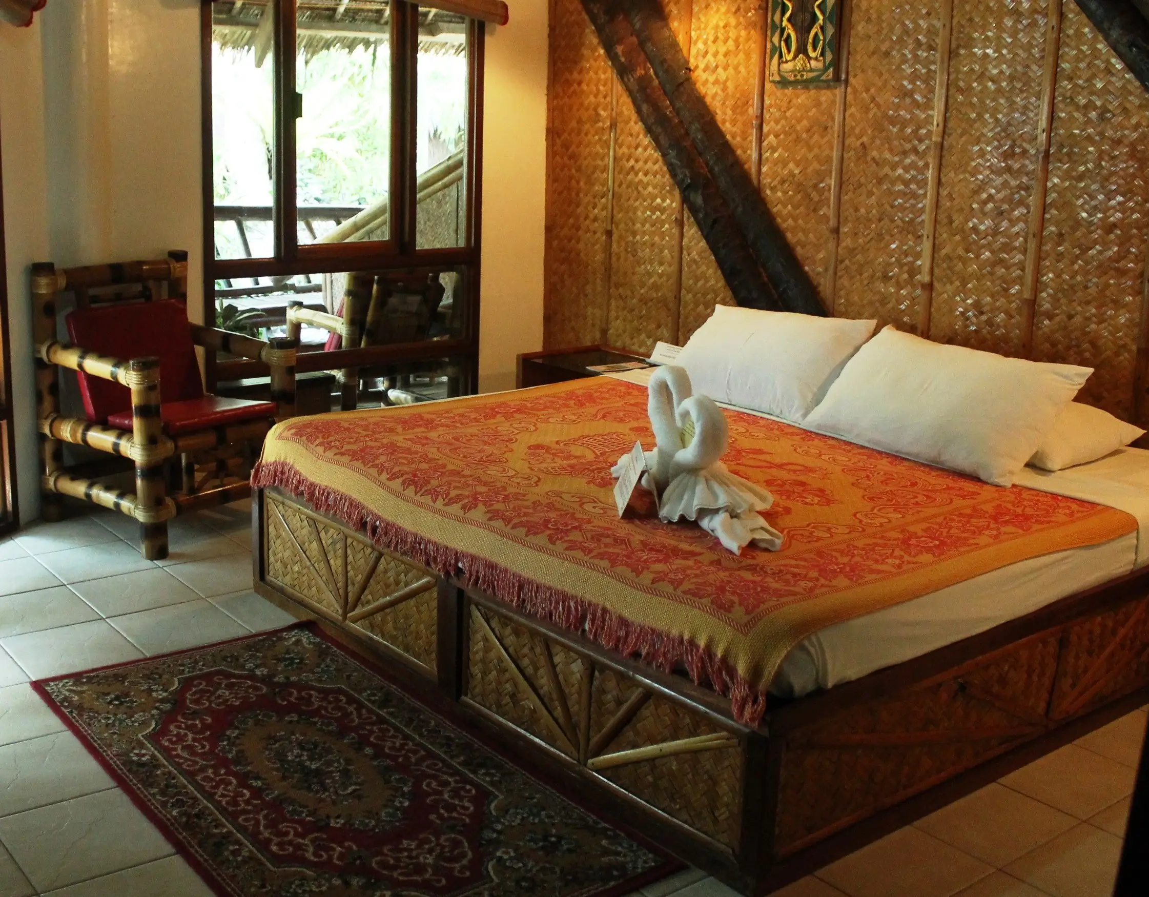 Cozy and inviting bedroom at Nigi Nigi Nu Noos Hotel in Boracay, featuring a bed with a red and gold patterned coverlet and white pillows.