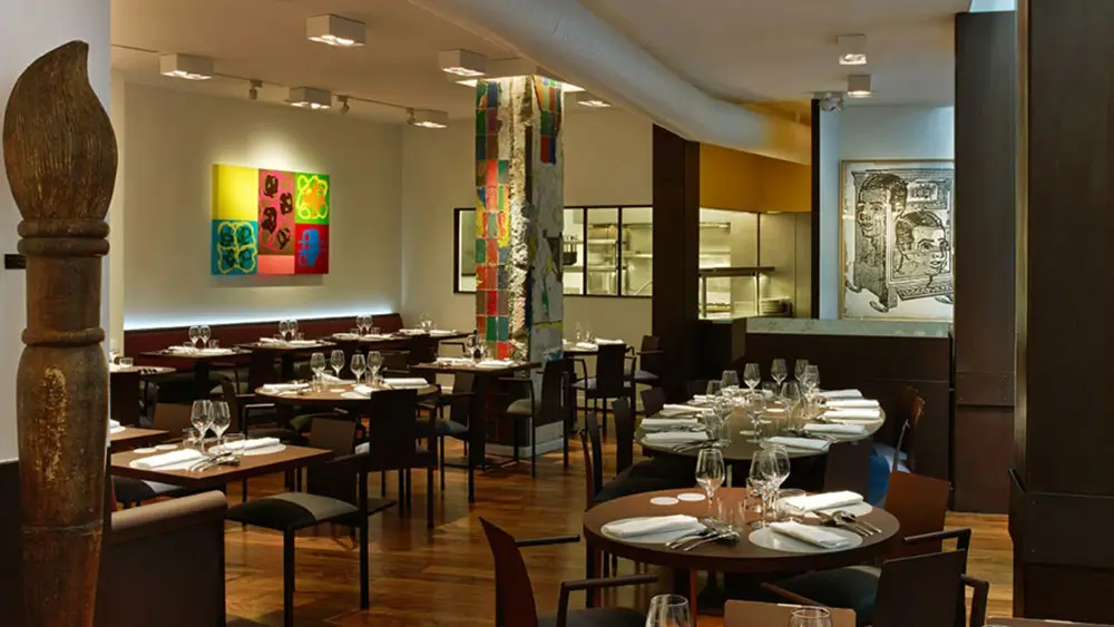 The interior of Ze Kitchen Galerie, an affordable Michelin star restaurant, featuring modern decor, colorful artwork, and elegantly set tables.