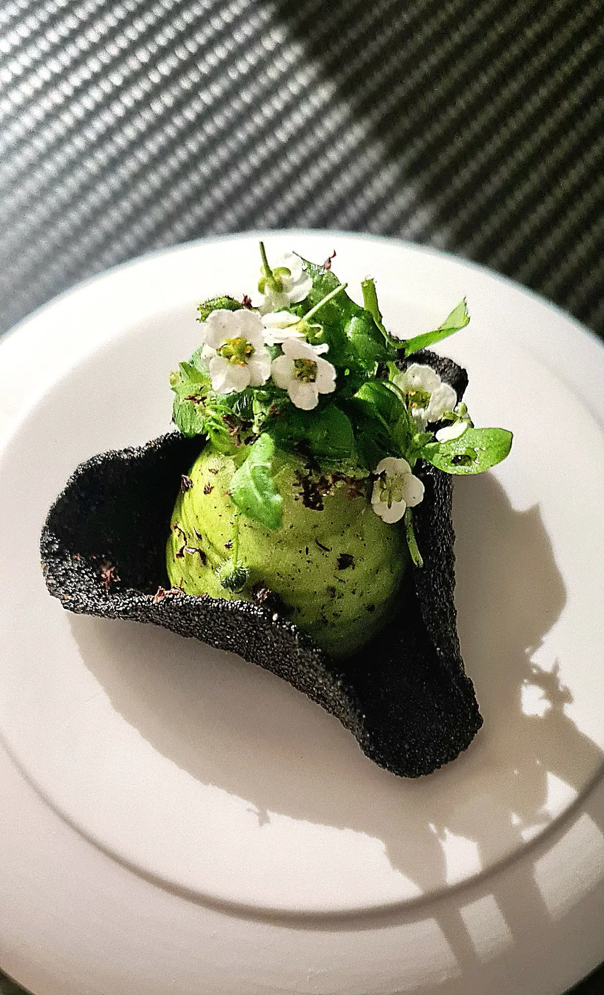 A beautifully presented dish at Restaurant Frederic Simonin in Paris, featuring a green scoop garnished with white flowers and crispy black elements.